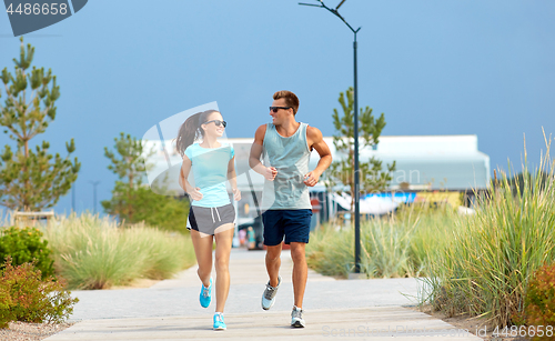 Image of couple in sports clothes running along beach path