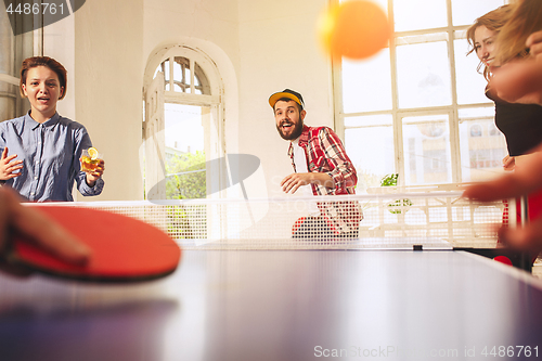 Image of Group of happy young friends playing ping pong table tennis