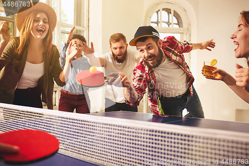 Image of Group of happy young friends playing ping pong table tennis