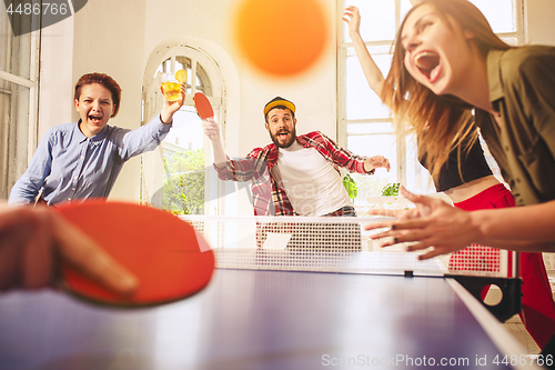 Image of Group of happy young friends playing ping pong table tennis