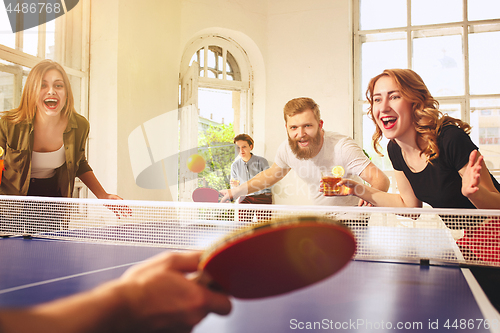 Image of Group of happy young friends playing ping pong table tennis