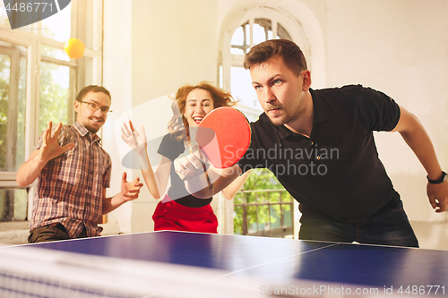 Image of Group of happy young friends playing ping pong table tennis