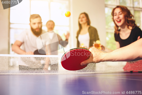 Image of Group of happy young friends playing ping pong table tennis