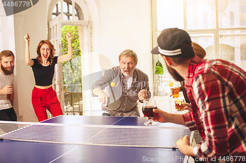 Image of Group of happy young friends playing ping pong table tennis