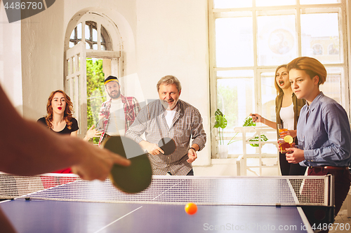 Image of Group of happy young friends playing ping pong table tennis