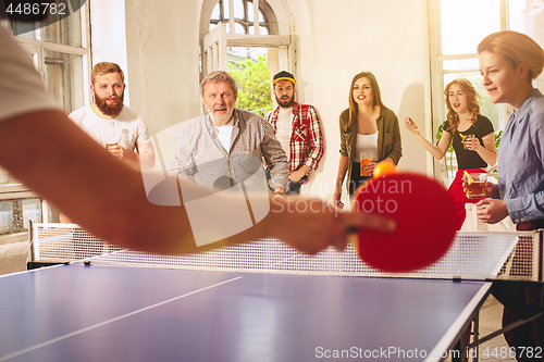 Image of Group of happy young friends playing ping pong table tennis