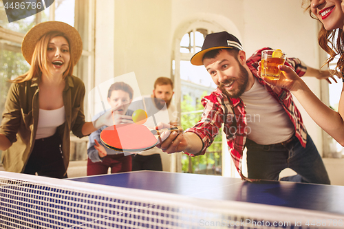 Image of Group of happy young friends playing ping pong table tennis