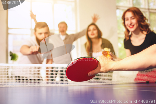 Image of Group of happy young friends playing ping pong table tennis