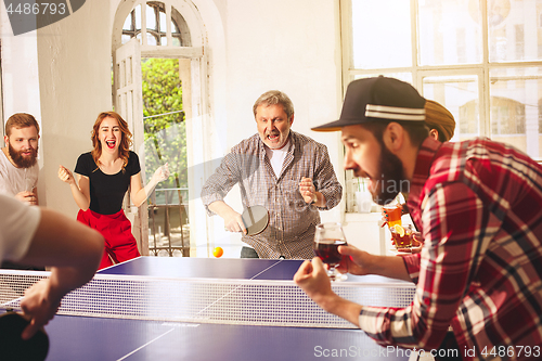 Image of Group of happy young friends playing ping pong table tennis