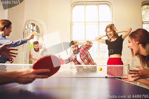 Image of Group of happy young friends playing ping pong table tennis