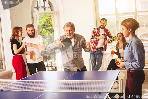 Image of Group of happy young friends playing ping pong table tennis