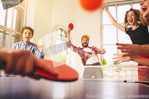 Image of Group of happy young friends playing ping pong table tennis