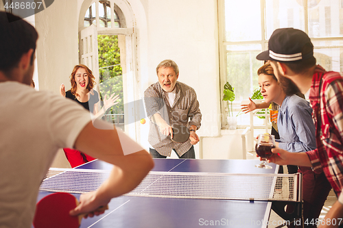 Image of Group of happy young friends playing ping pong table tennis