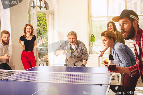 Image of Group of happy young friends playing ping pong table tennis