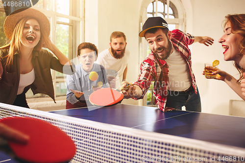 Image of Group of happy young friends playing ping pong table tennis