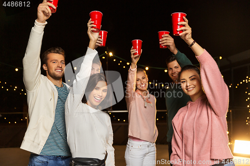 Image of friends toasting party cups on rooftop at night