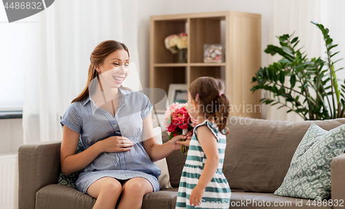 Image of girl giving flowers to her pregnant mother at home