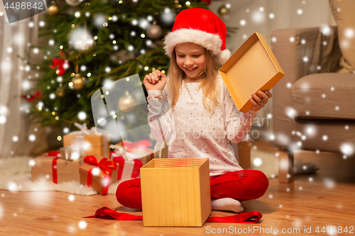 Image of excited girl in santa hat opening christmas gift