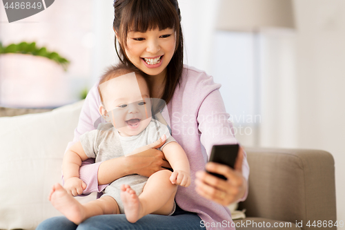 Image of asian mother with baby son taking selfie at home