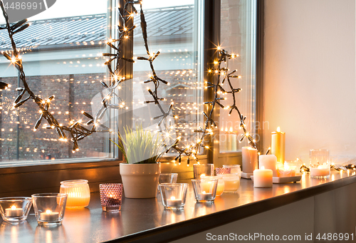 Image of candles burning on window sill with garland lights