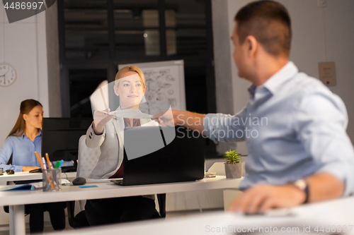 Image of woman giving papers to colleague at night office