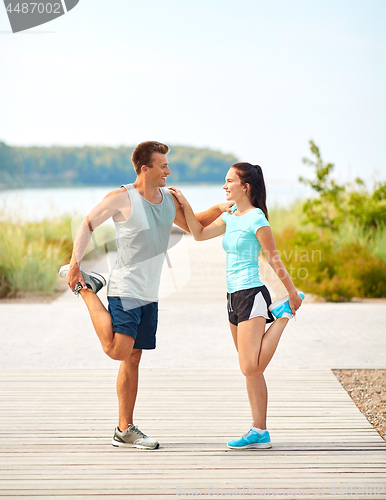 Image of smiling couple stretching legs on beach