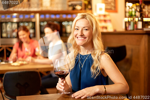 Image of happy woman drinking red wine at bar or restaurant