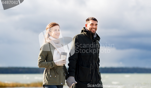 Image of couple with tumbler walking along autumn beach