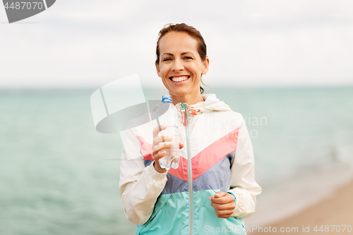 Image of woman drinking water after exercising on beach