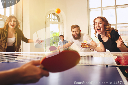 Image of Group of happy young friends playing ping pong table tennis