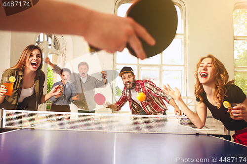 Image of Group of happy young friends playing ping pong table tennis