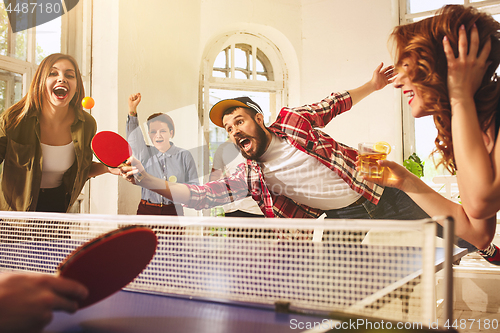 Image of Group of happy young friends playing ping pong table tennis