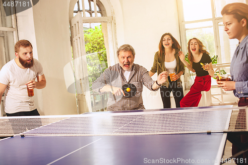 Image of Group of happy young friends playing ping pong table tennis