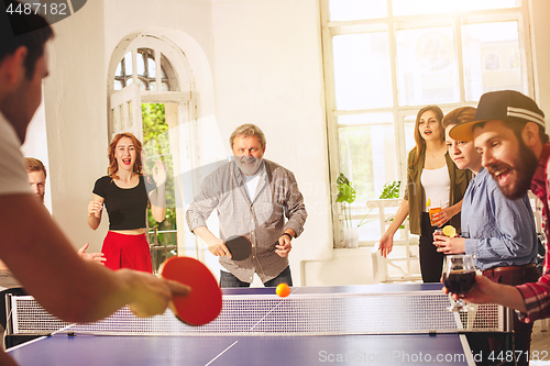 Image of Group of happy young friends playing ping pong table tennis