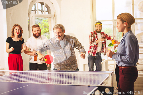 Image of Group of happy young friends playing ping pong table tennis