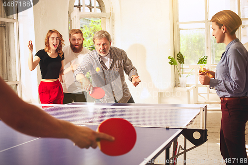 Image of Group of happy young friends playing ping pong table tennis