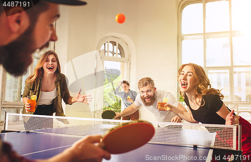 Image of Group of happy young friends playing ping pong table tennis