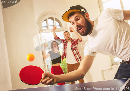 Image of Group of happy young friends playing ping pong table tennis