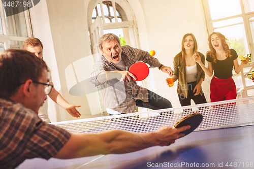 Image of Group of happy young friends playing ping pong table tennis