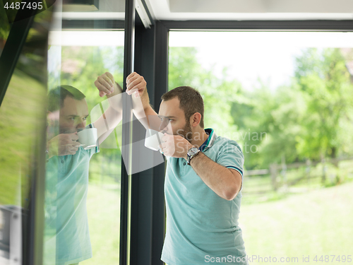 Image of young man drinking morning coffee by the window