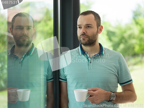 Image of young man drinking morning coffee by the window