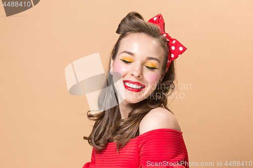 Image of Beautiful young woman with pinup make-up and hairstyle. Studio shot on pastel background