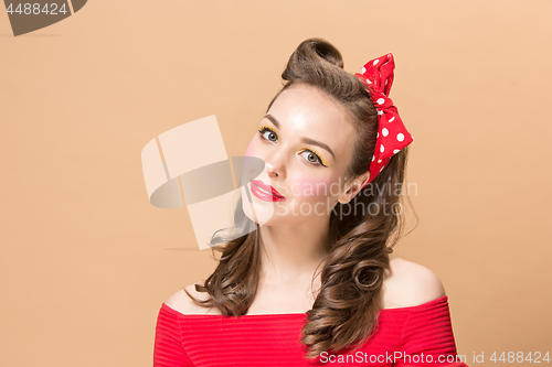 Image of Beautiful young woman with pinup make-up and hairstyle. Studio shot on pastel background