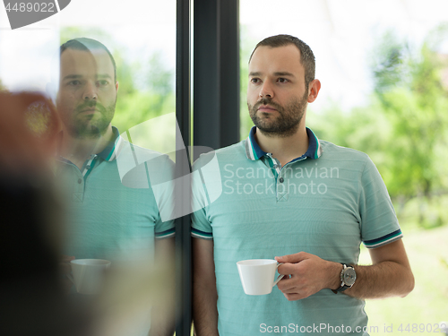 Image of young man drinking morning coffee by the window