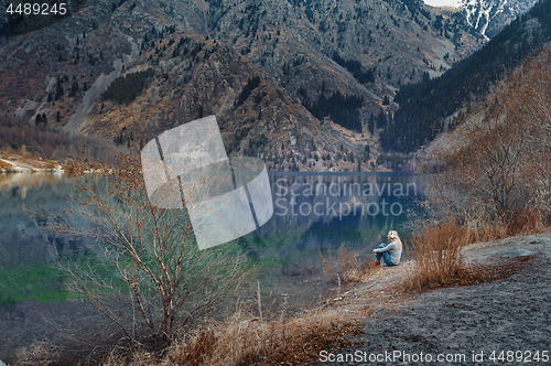 Image of Woman listening music at the water's edge of mountain lake