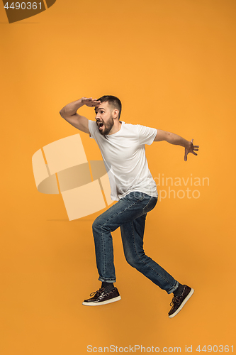 Image of Freedom in moving. handsome young man jumping against orange background