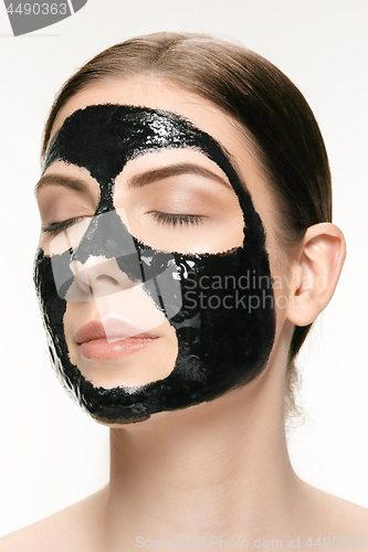 Image of Young beautiful woman applying a mask for the face of the therapeutic black mud. Spa treatment