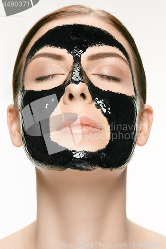 Image of Young beautiful woman applying a mask for the face of the therapeutic black mud. Spa treatment