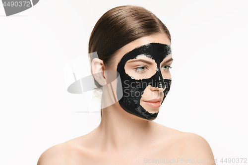 Image of Young beautiful woman applying a mask for the face of the therapeutic black mud. Spa treatment