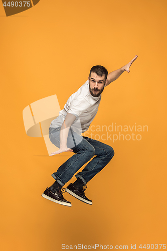 Image of Freedom in moving. handsome young man jumping against orange background